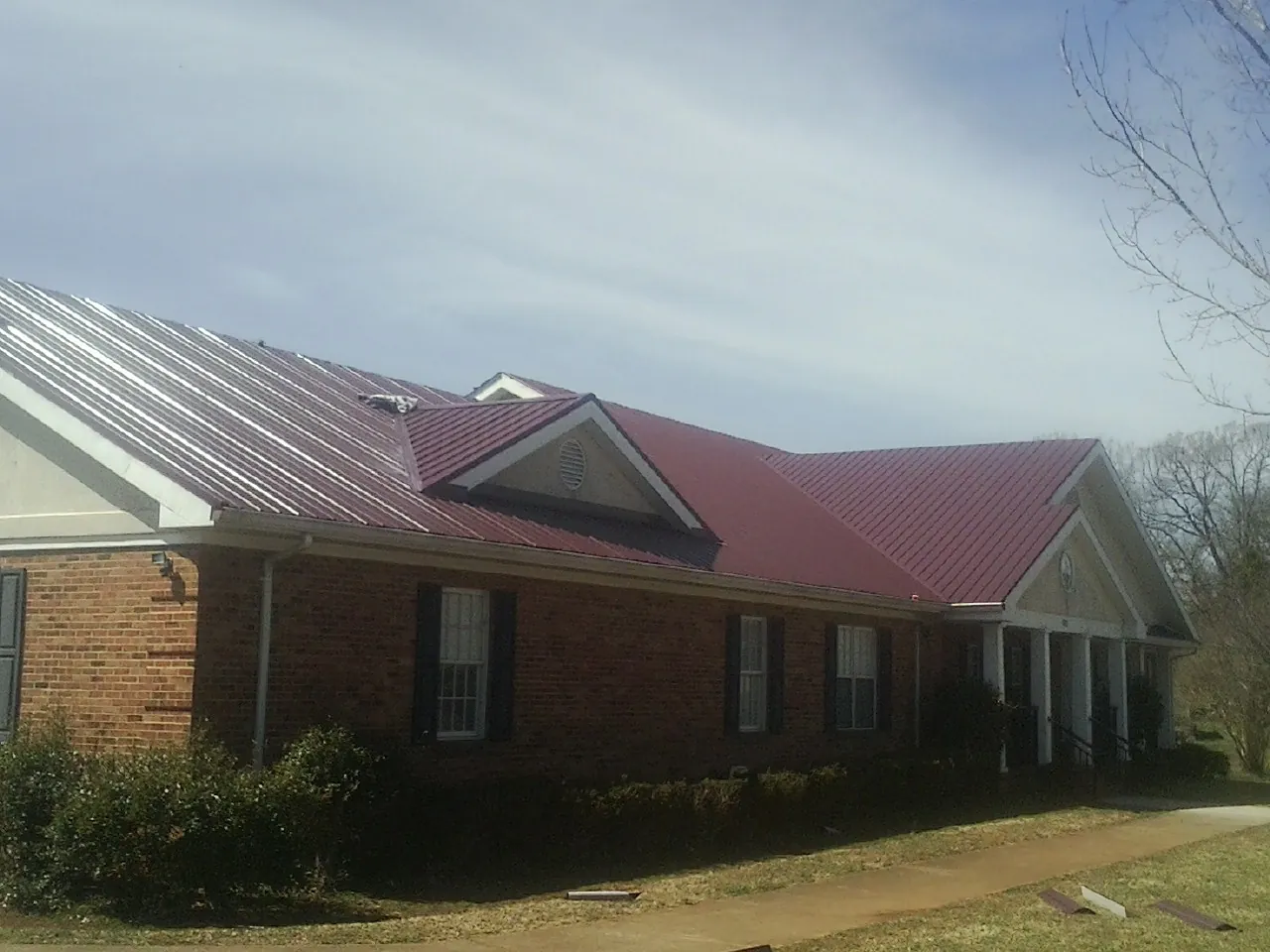 Red metal roof with gabled entries on a long brick building, from a Hail Damage Roof Repair job in Cortez